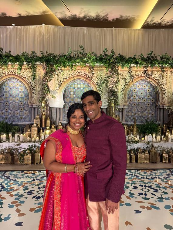 Manu and Nikhil in Indian wedding outfits in front of tiled arches
