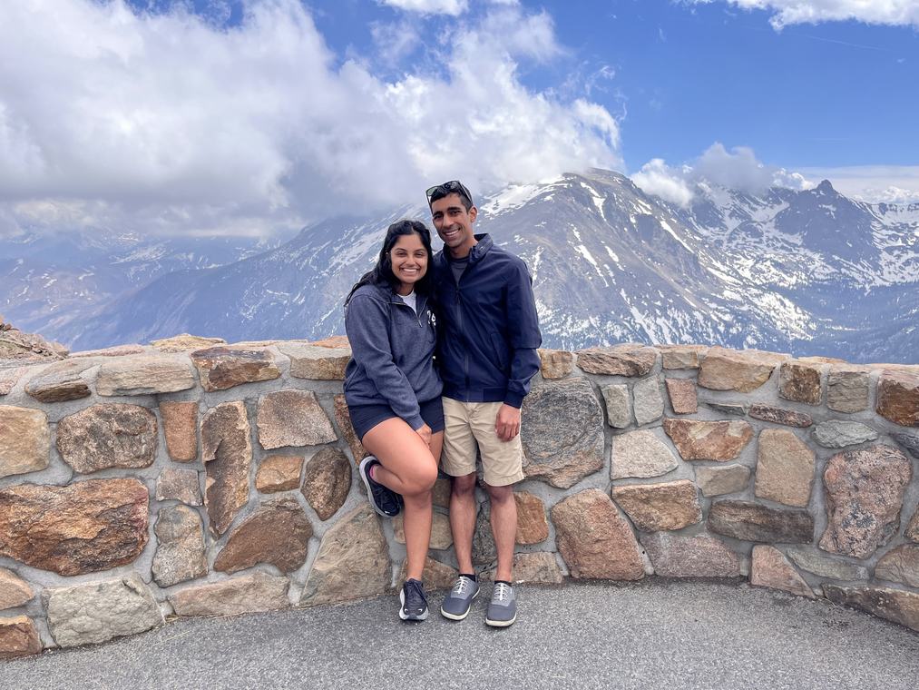 Manu and Nikhil at a stone wall overlook with snowy peaks behind them